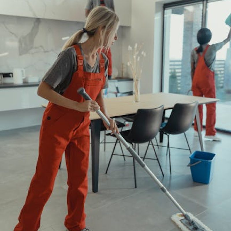 Cleaning team in red overalls mopping and sanitizing a modern home interior.